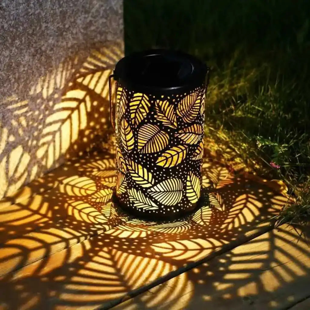 Farol solar encendido proyectando sombras de hojas en el suelo, ideal para iluminar terrazas o jardines con estilo natural.