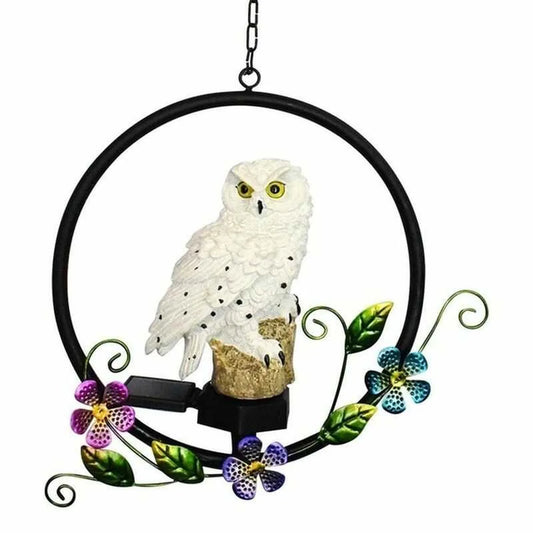 Lámpara solar decorativa con figura de búho blanco sobre aro metálico con flores, ideal para jardín o terraza exterior.