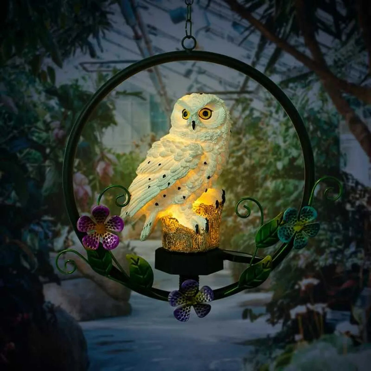 Lámpara solar de búho iluminado en jardín nocturno con luz cálida, decoración exterior elegante con aro metálico y flores.