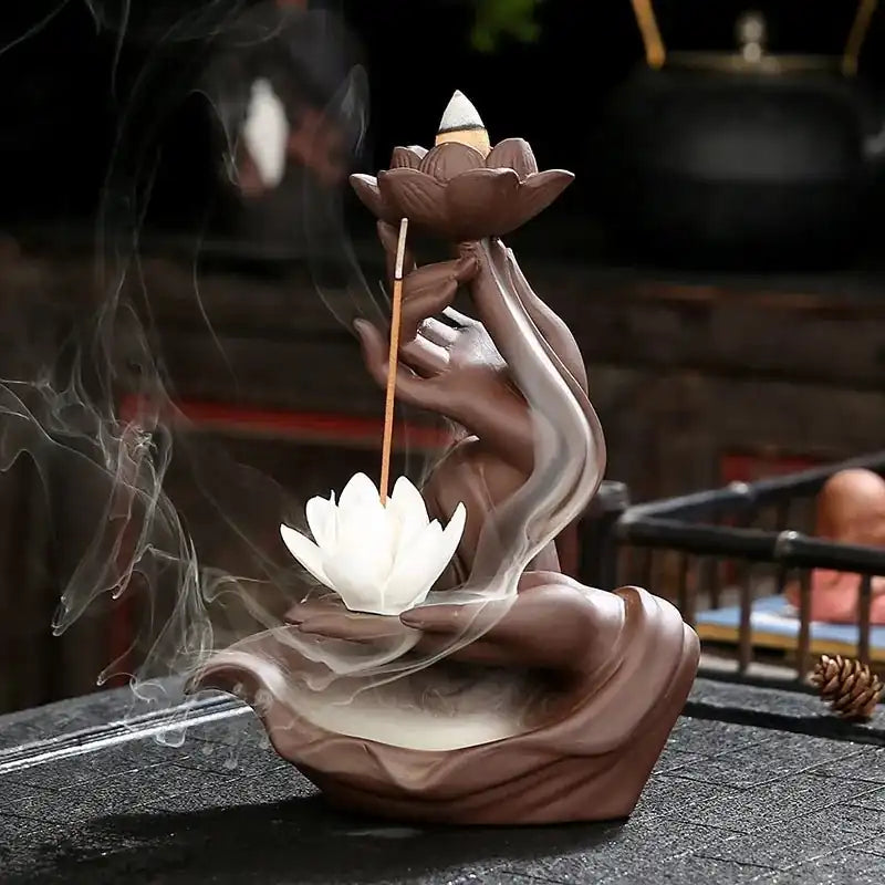 Porta incienso con forma de mano sosteniendo flor de loto y varilla, humo efecto cascada en ambiente zen interior.