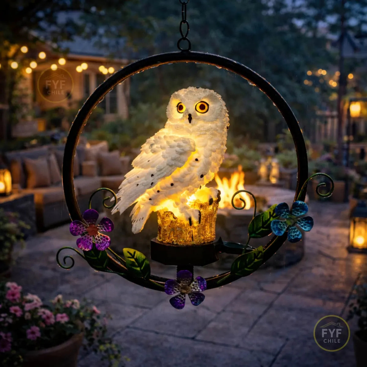 Colgante solar de búho LED iluminado en terraza de jardín durante la noche con luces cálidas y fogón de fondo