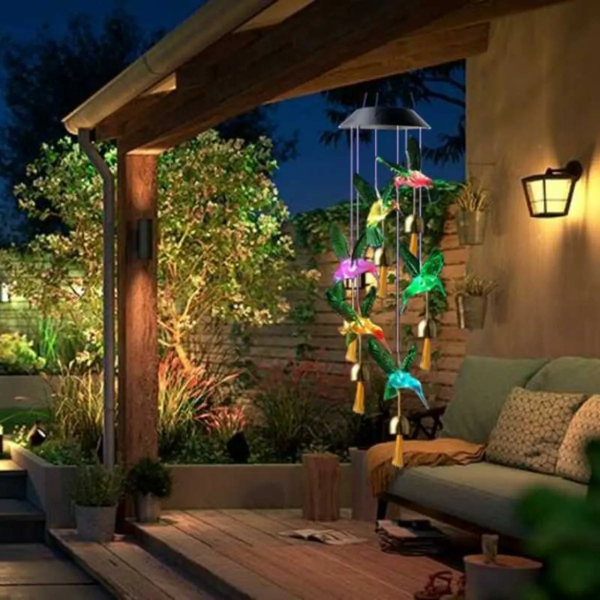 Colgante solar de colibríes LED multicolor iluminando una terraza exterior de noche, ideal para jardín, patio o balcón.