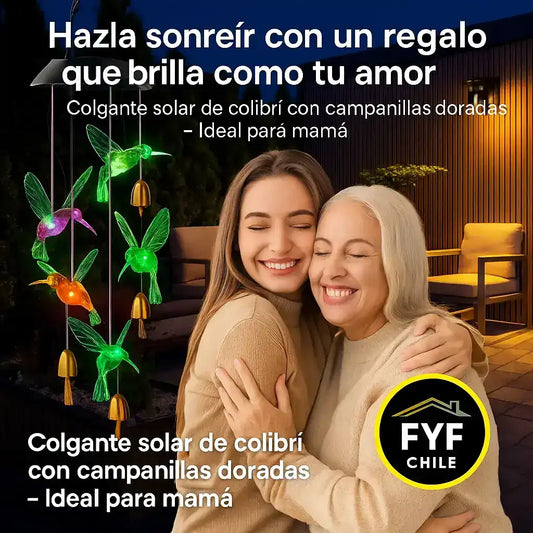 Mamá e hija abrazadas con colgante solar de colibrí iluminado al fondo, regalo emocional con campanillas doradas para el jardín.