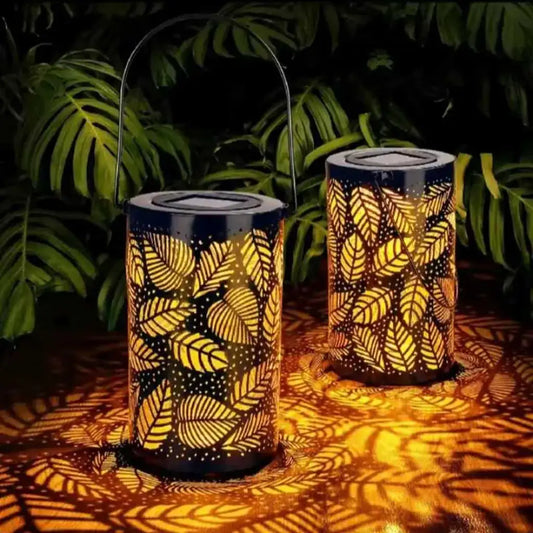 Farol solar decorativo encendido de noche con diseño de hojas proyectadas en el suelo, ideal para jardín o terraza