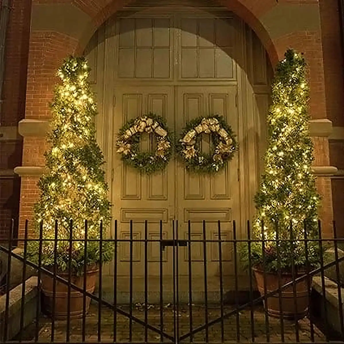 Luces solares decorativas en entrada de casa con árboles iluminados y coronas navideñas en la puerta