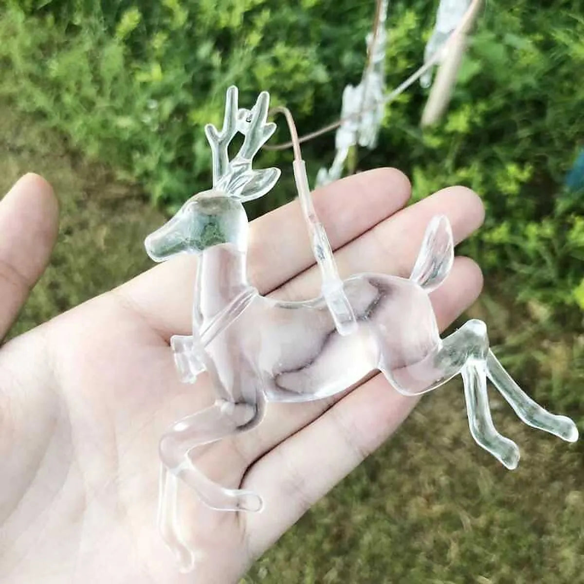 Detalle de reno transparente para colgante solar LED decorativo de jardín sostenido en la mano