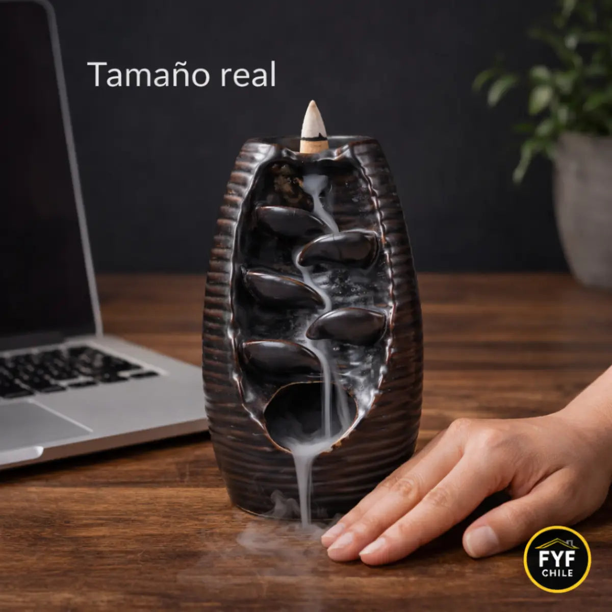 comparación de tamaño real del porta incienso cascada backflow de cerámica sobre escritorio junto a mano y computador portátil para referencia de escala